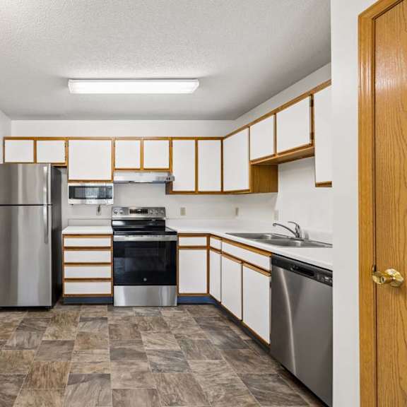Thumbnail 11 of 23 Apartment kitchen with white and wood-tone cabinetry, stainless steel refrigerator and dishwasher, black oven, laminate countertops, and a functional U-shaped layout with a pass-through opening.