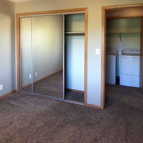 Thumbnail 4 of 6 A bedroom with a carpeted floor, a sliding mirror door closet, and a door open to the hallway with a view of the laundry room.