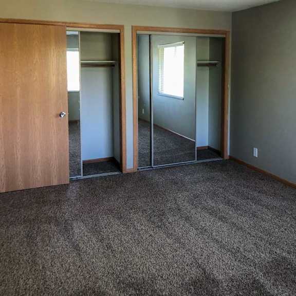 Thumbnail 5 of 6 A bedroom with a carpeted floor, two mirrored-door closets, and a large window.
