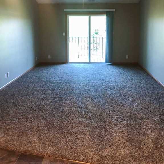 Thumbnail 3 of 6 A living room with a carpeted floor and a sliding glass door to the balcony.
