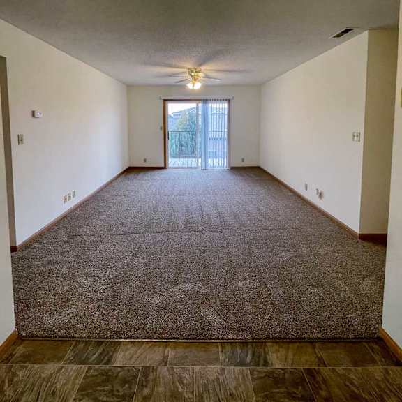 Thumbnail 2 of 10 A living room with carpeted flooring, a ceiling fan, and a sliding glass door to a balcony.