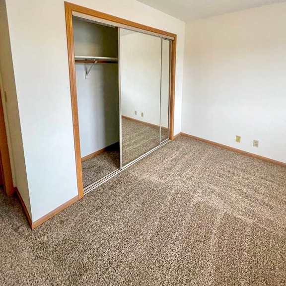 Thumbnail 3 of 10 A bedroom with a carpeted floor and a sliding mirror door closet.