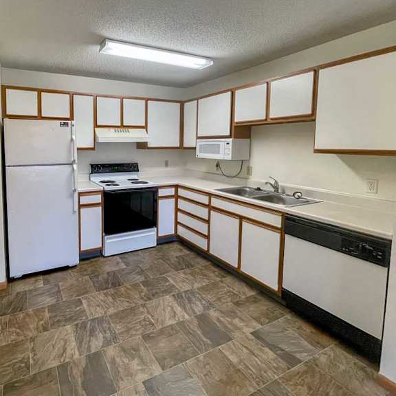Thumbnail 4 of 10 A kitchen with white appliances and white cabinets with oak colored trim.