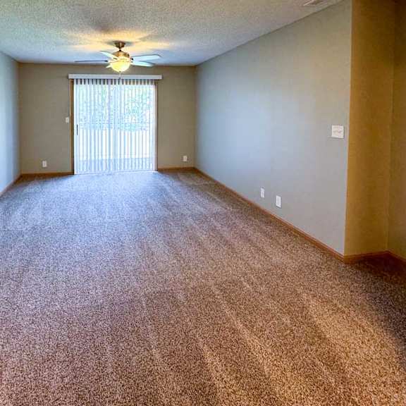 Thumbnail 6 of 10 A living room with a carpeted floor, sliding glass door to a balcony, and a ceiling fan.