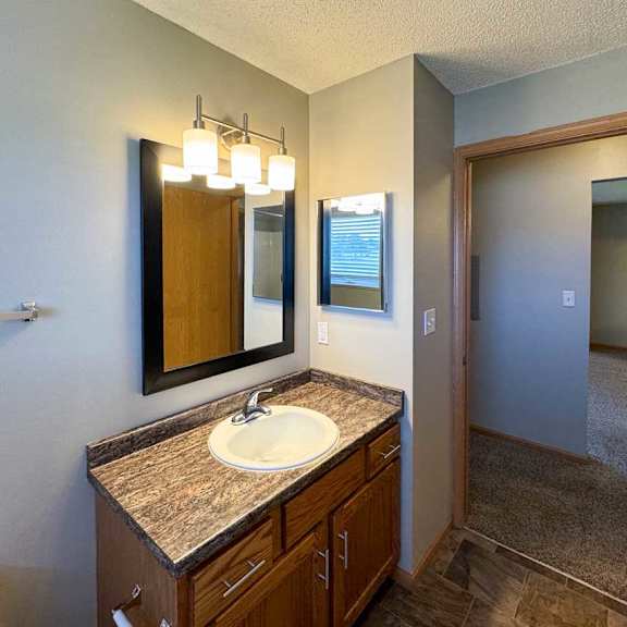Thumbnail 9 of 10 A bathroom with a granite vanity sink, mirror, medicine cabinet, and overhead lighting.