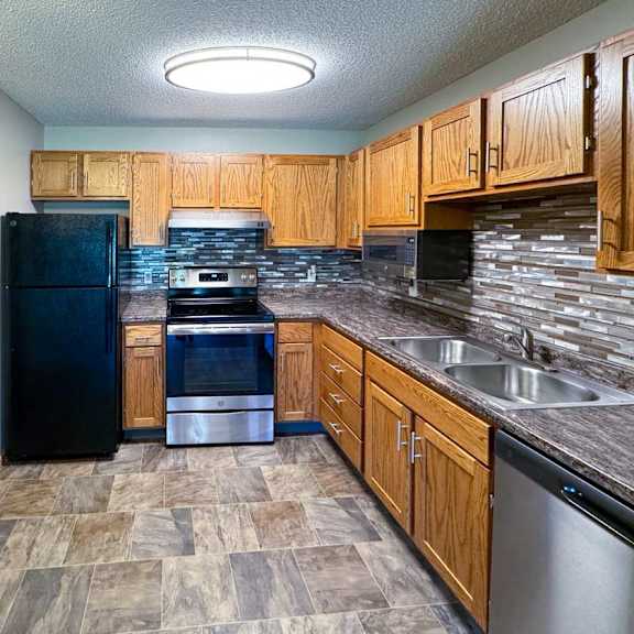 Thumbnail 7 of 10 An updated kitchen with wooden cabinets, black and stainless steel appliances, granite countertops, and a tile backsplash.