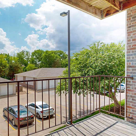 Thumbnail 12 of 28 a covered balcony with a metal railing, overlooking detached garages and green trees
