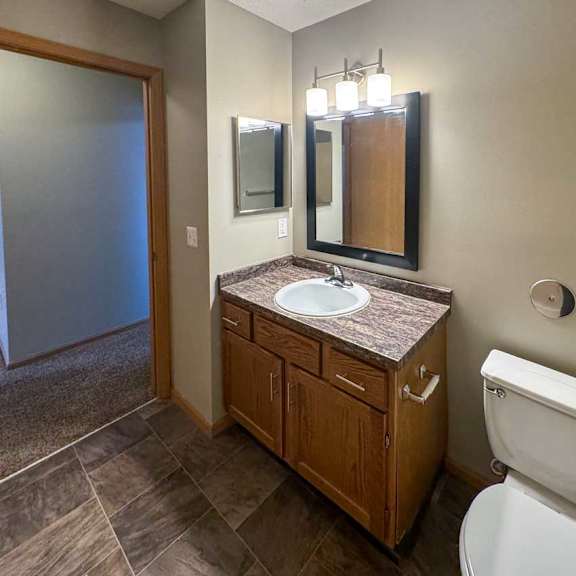 Thumbnail 7 of 9 A bathroom with a granite vanity sink, a framed mirror with overhead lighting, and a medicine cabinet.