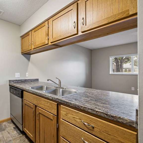 Thumbnail 23 of 29 Apartment kitchen with wood cabinetry, black appliances, a double-basin sink, laminate countertops, and a pass-through opening connecting to the living area.