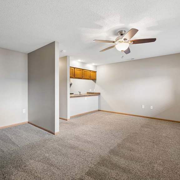 Thumbnail 20 of 29 Spacious apartment living room with carpeted flooring, a ceiling fan, a pass-through to the kitchen, and a window with blinds providing natural light.