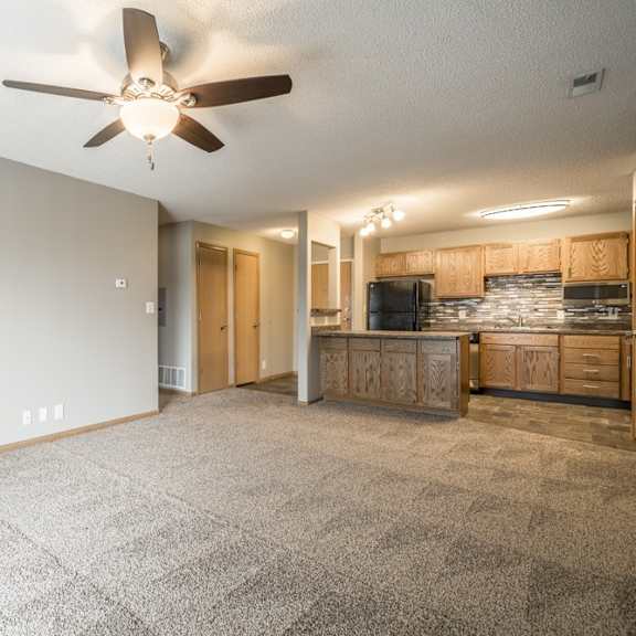 Thumbnail 2 of 14 a spacious living room with a ceiling fan and a kitchen area in the background