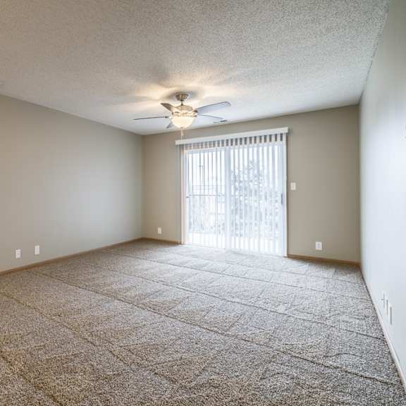 Thumbnail 7 of 14 a carpeted living room with a ceiling fan and a sliding glass door to a balcony