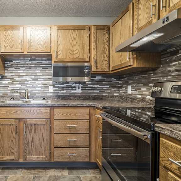 Thumbnail 4 of 14 a kitchen with wooden cabinets, a tile backsplash, granite countertops, and stainless steel appliances