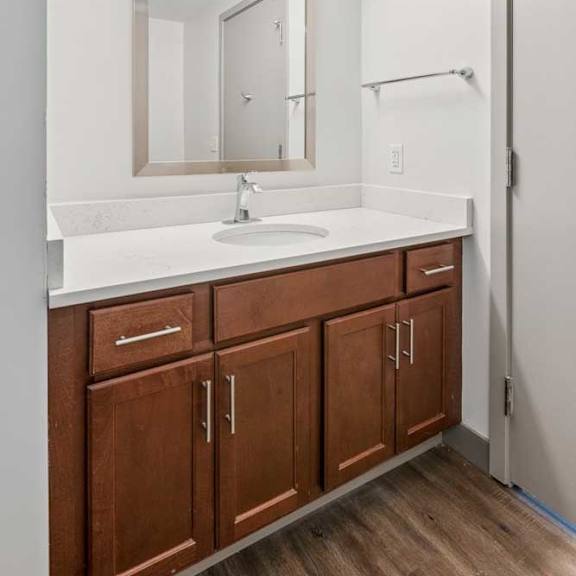 Thumbnail 17 of 19 A bathroom with wooden cabinets, a white granite vanity sink, and a framed mirror with overhead lighting.