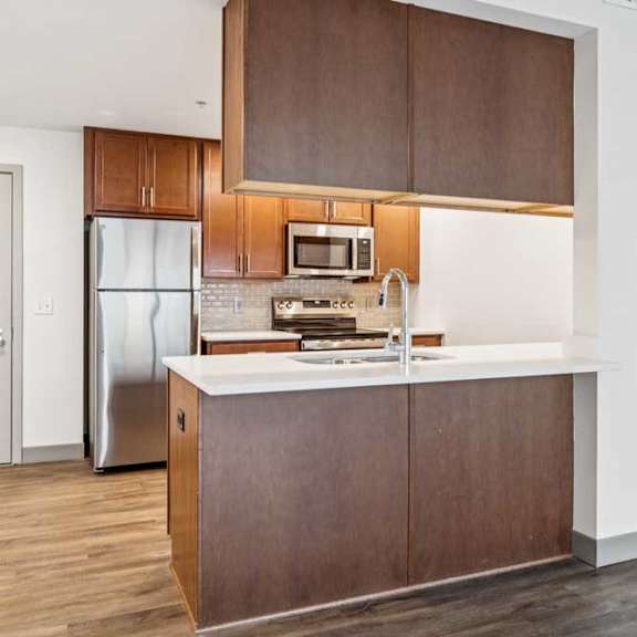 Thumbnail 4 of 19 A modern kitchen with wooden cabinets, granite countertops, a tile backsplash, stainless steel appliances, and a peninsula with overhead cabinets.