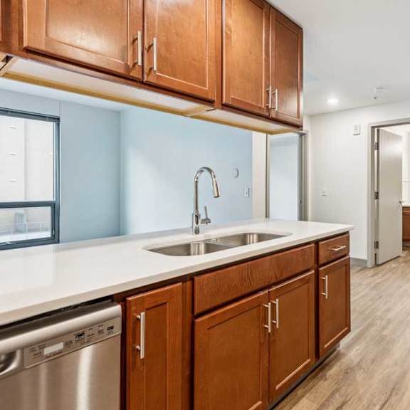 Thumbnail 6 of 19 A kitchen peninsula with overhead wooden cabinets, granite countertops, and stainless steel appliances, in front of a living room.