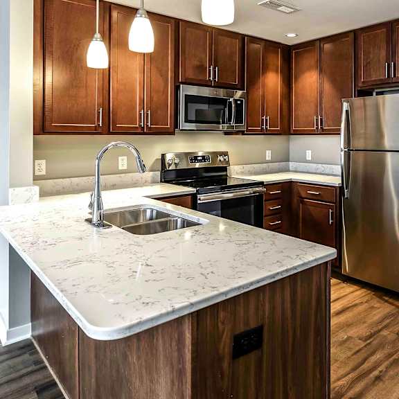 Thumbnail 2 of 9 Full view of the kitchen with dark wood flooring and cabinets, stainless steel appliances and white quartz countertops in a one bedroom apartment at Midtown Crossing apartments