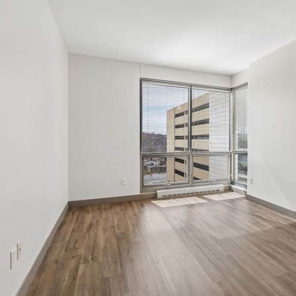 Thumbnail 10 of 11 A room with wooden floors and a large window overlooking a building.