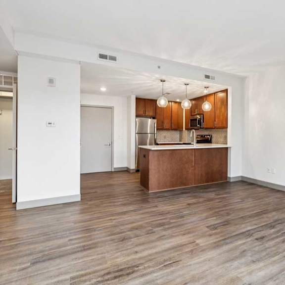 Thumbnail 8 of 16 A living room with hardwood-style flooring the opens to a modern kitchen.