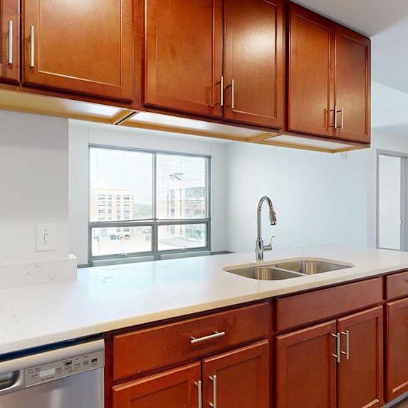 Thumbnail 7 of 24 A kitchen with warm wooden cabinets, and a peninsula counter with sink overlooking a living room.