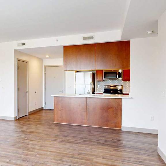 Thumbnail 2 of 24 A living room with hardwood-style flooring and kitchen with warm wooden cabinets.