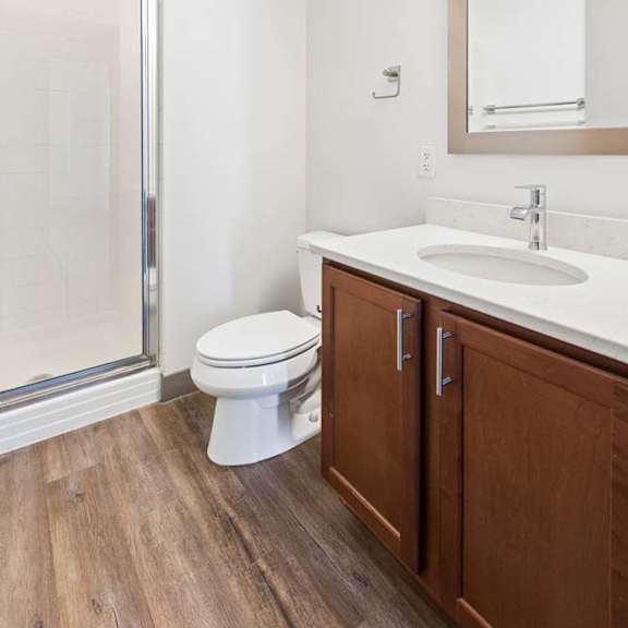 Thumbnail 12 of 20 A white toilet sits in a bathroom with a wooden cabinet and a mirror above the sink.