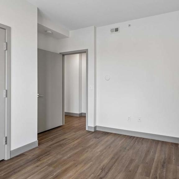 Thumbnail 18 of 19 A room with white walls and wooden flooring with two doors.