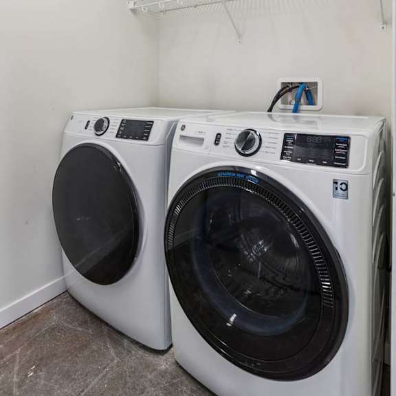 Thumbnail 4 of 19 Two white front load washing machines in a laundry room.