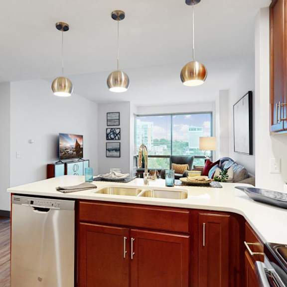 Thumbnail 4 of 14 A kitchen with brown cabinets and a white countertop looking into living room