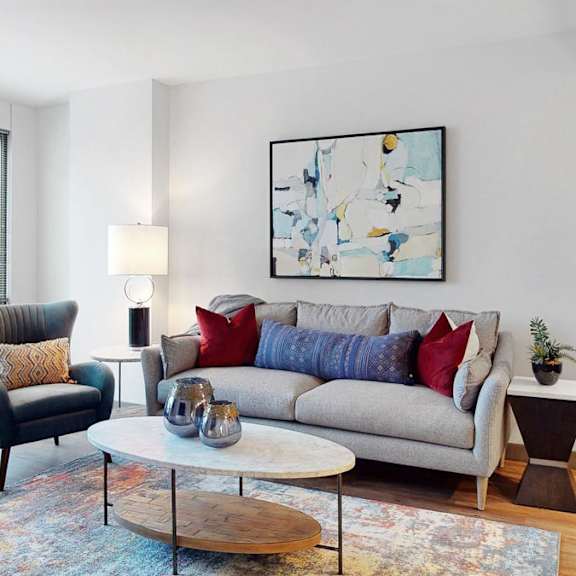 Thumbnail 6 of 14 A living room with a grey couch, a black chair, a wooden coffee table, and large windows
