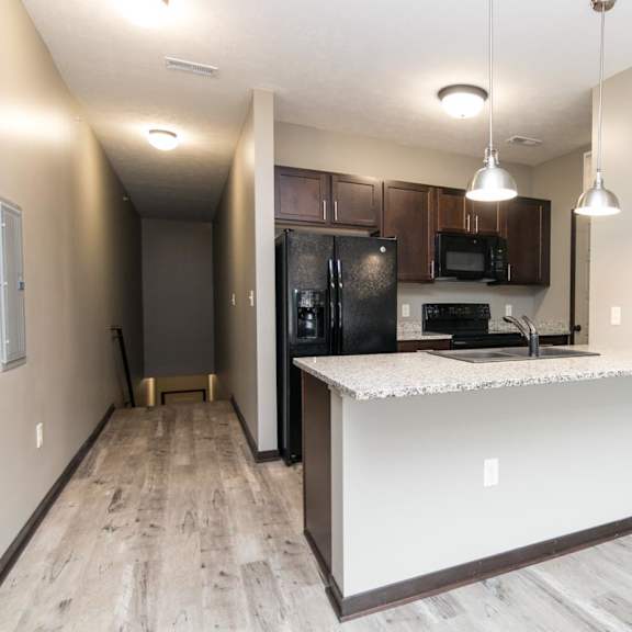 Thumbnail 5 of 9 A kitchen with a black fridge and microwave, brown cabinets, and a white countertop.