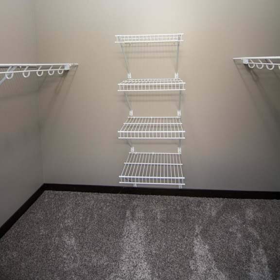 Thumbnail 7 of 13 A walk-in closet with three white shelves on the wall.