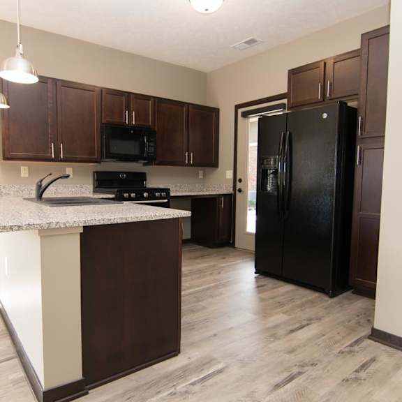 Thumbnail 2 of 13 A kitchen with a black refrigerator and brown cabinets.