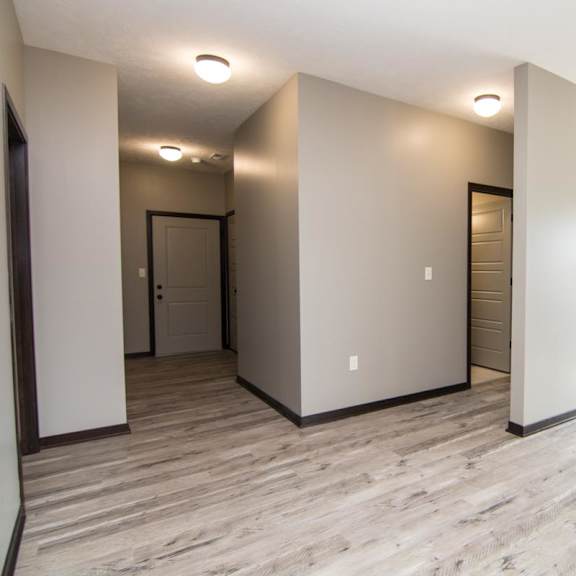 Thumbnail 5 of 13 A spacious living room with light brown flooring and white walls.