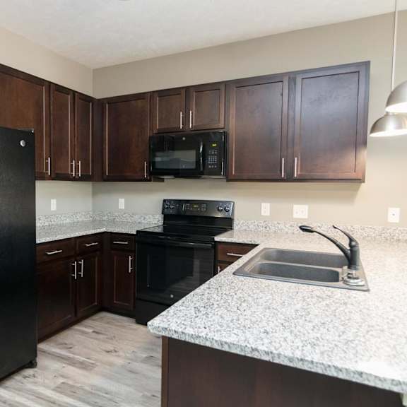 Thumbnail 3 of 14 A black fridge and microwave in a kitchen with brown cabinets.