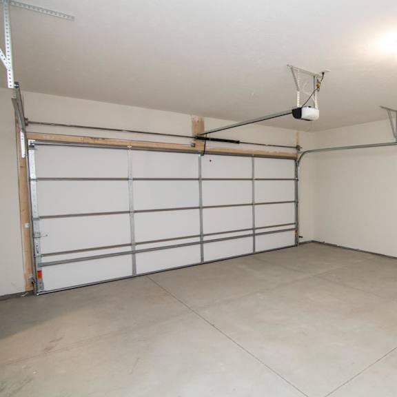 Thumbnail 14 of 14 A large empty garage with a white door and a grey floor.