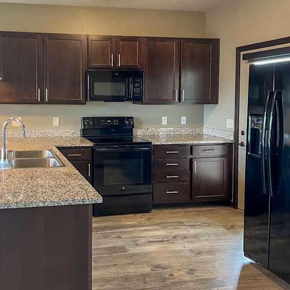 Thumbnail 5 of 20 a kitchen with dark wood cabinets, granite countertops, and black appliances