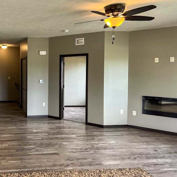 Thumbnail 8 of 20 a living room with hard wood flooring, a fireplace, a ceiling fan, and a door to the den space