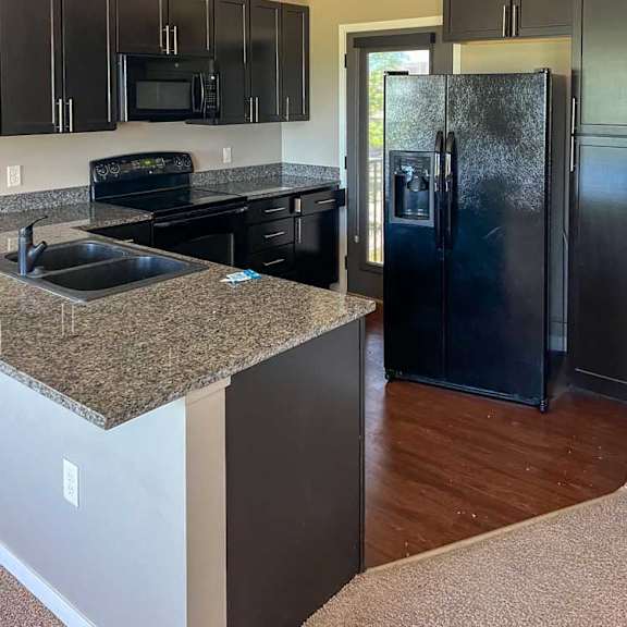 Thumbnail 9 of 15 a kitchen with dark wooden cabinets, granite countertops, hardwood flooring, and black appliances