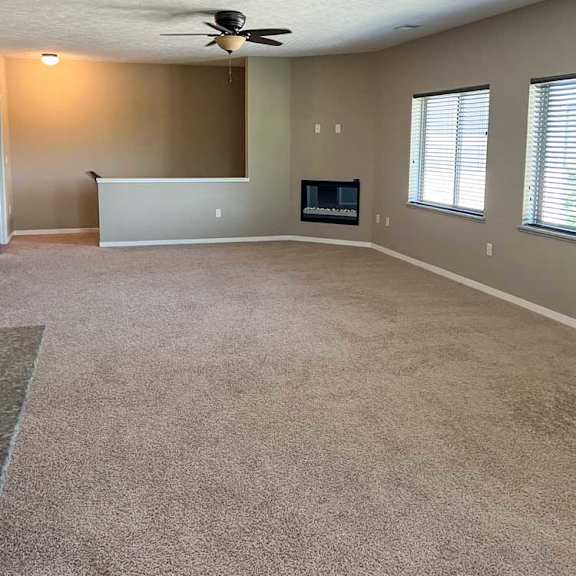 Thumbnail 5 of 15 a living room with carpeted flooring, several windows, a ceiling fan, and a fireplace