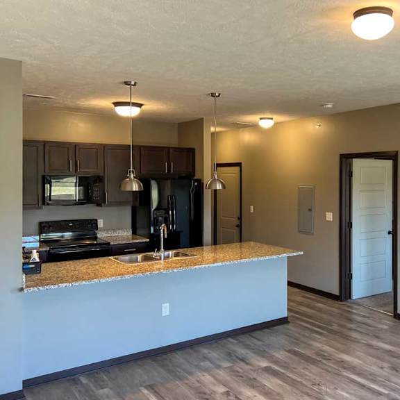 Thumbnail 20 of 35 a kitchen with dark wooden cabinets, granite countertops, and black appliances featuring a large peninsula countertop