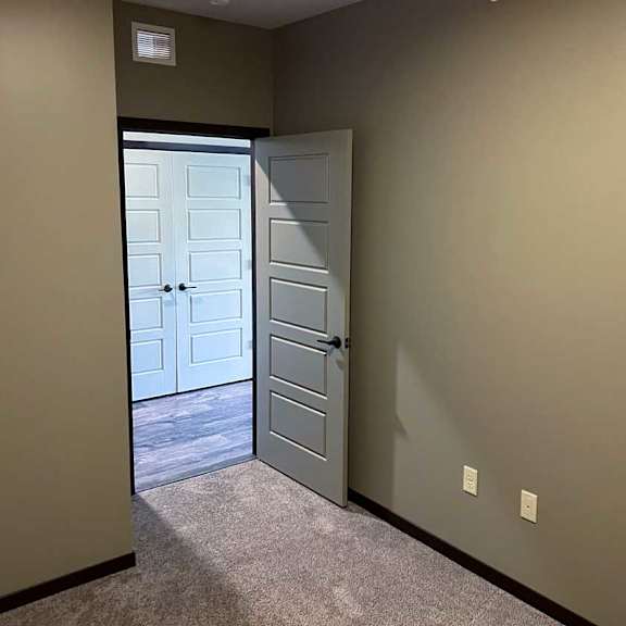 Thumbnail 4 of 19 a den with carpeted flooring and a door leading to the front entry hallway