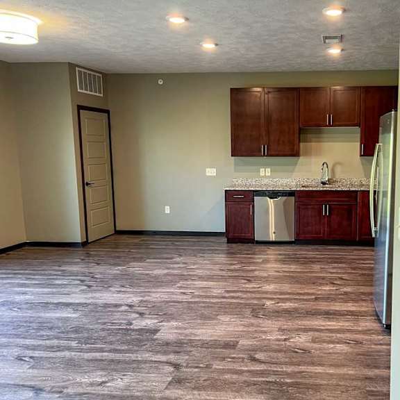 Thumbnail 8 of 19 an open-concept living room and kitchen with red-brown cabinets and hard wood flooring