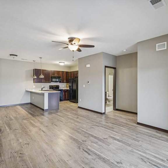 Thumbnail 24 of 33 A spacious room with a ceiling fan and a kitchen area in the background.