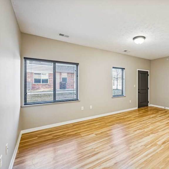 Thumbnail 12 of 18 A large living room with wooden floors and large windows. The front door is dark and on the right.