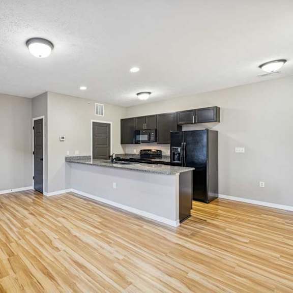 Thumbnail 11 of 18 An apartment kitchen with wooden floors, black appliances, and granite countertops..