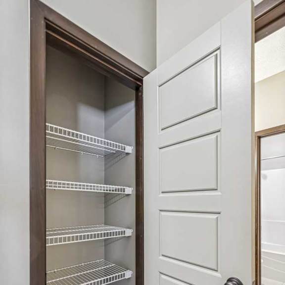 Thumbnail 27 of 45 Apartment storage closet with white wire shelving, wood-style flooring, and a paneled door, located near a bathroom with tile flooring and a visible bathtub.