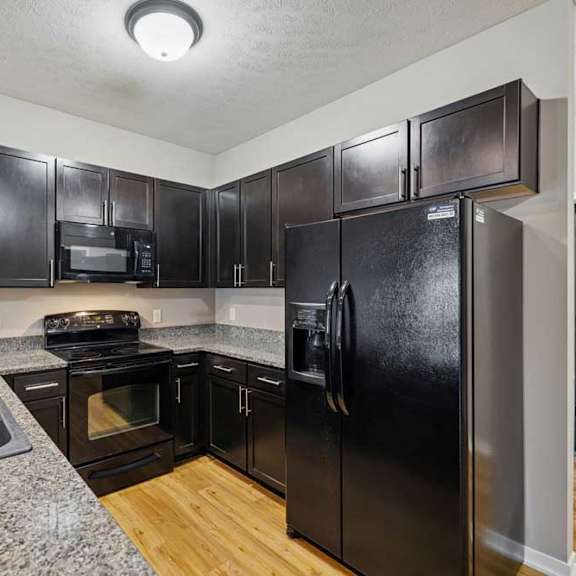 Thumbnail 6 of 45 A kitchen with dark wooden cabinets, granite countertops, and black-finish appliances.