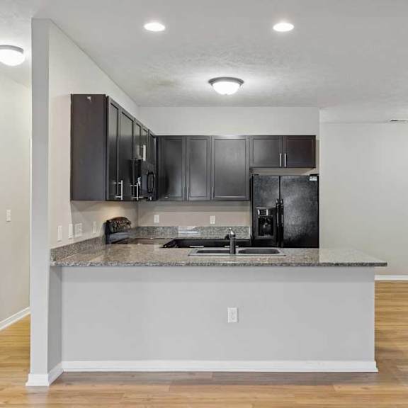 Thumbnail 5 of 45 A kitchen with dark wooden cabinets, granite countertops, black appliances, and a peninsula countertop.