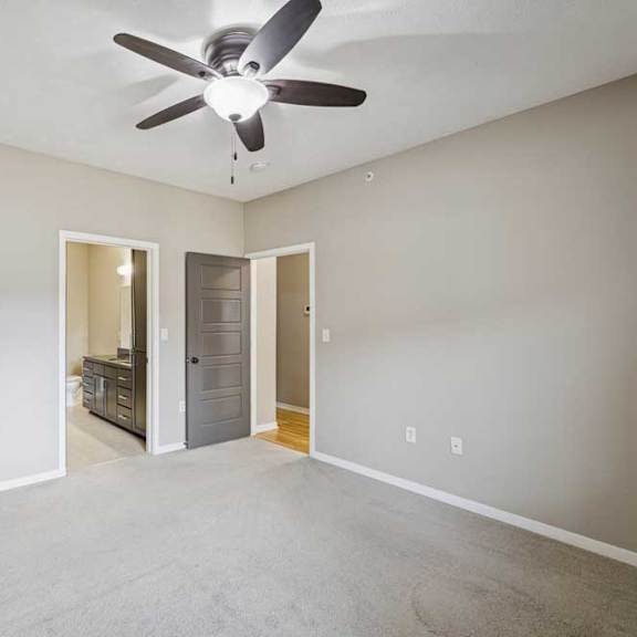 Thumbnail 11 of 22 A carpeted bedroom with an attached bathroom, a ceiling fan, and a door open to the living room.